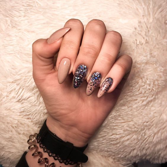 Vernis à ongles nude avec des paillettes noires sur de longs ongles en amande