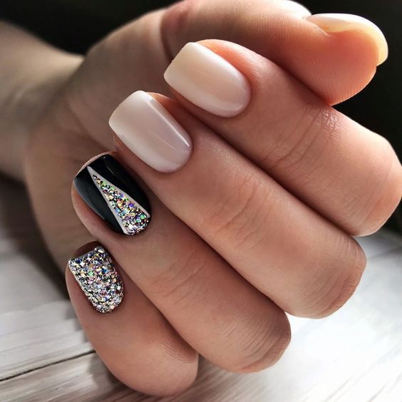 Vernis à ongles nude pâle et noir avec des paillettes argentées sur des ongles carrés courts et effilés