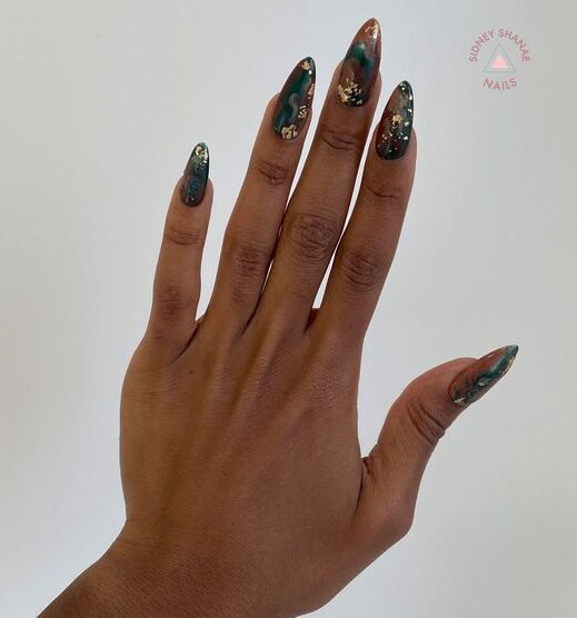 Nail art en marbre fumé vert foncé avec des accents de feuille d’or sur une longue presse en forme d’amande sur les ongles