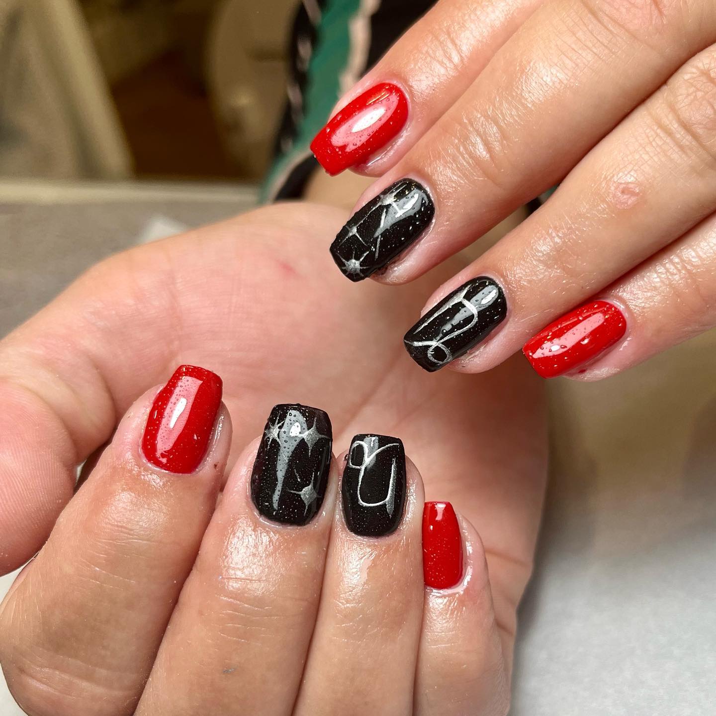 Couleurs d’ongles noires et rouges vibrantes avec le symbole du Capricorne nail art sur des ongles carrés courts et effilés