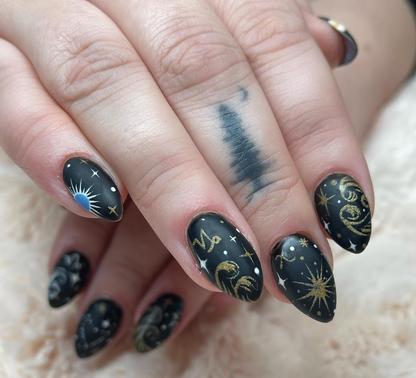 Vernis à ongles noir au fini mat avec symbole du Capricorne et motifs d’ongles célestes sur ongles en amande moyenne