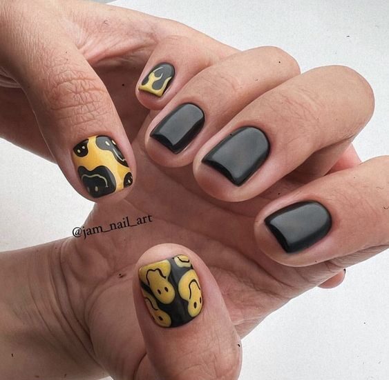 Couleurs d’ongles noires et jaunes avec des visages souriants sur des ongles carrés courts