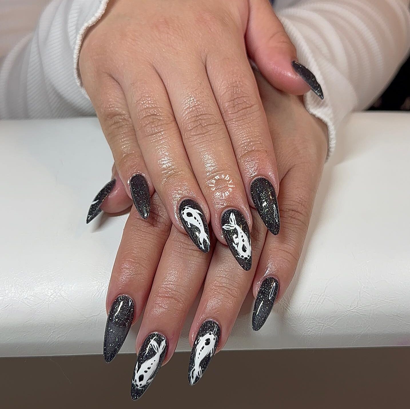 Couleur d’ongle noire avec paillettes et arts d’ongles de poisson koi sur de longs ongles en amande