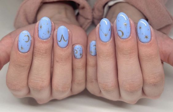 Couleur d’ongles bleu ciel avec signe Bélier doré et éléments célestes nail arts sur ongles ronds moyens