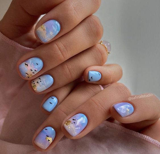 Vernis à ongles bleu clair avec des arts d’ongles abstraits et des accents de feuille d’or sur les ongles courts