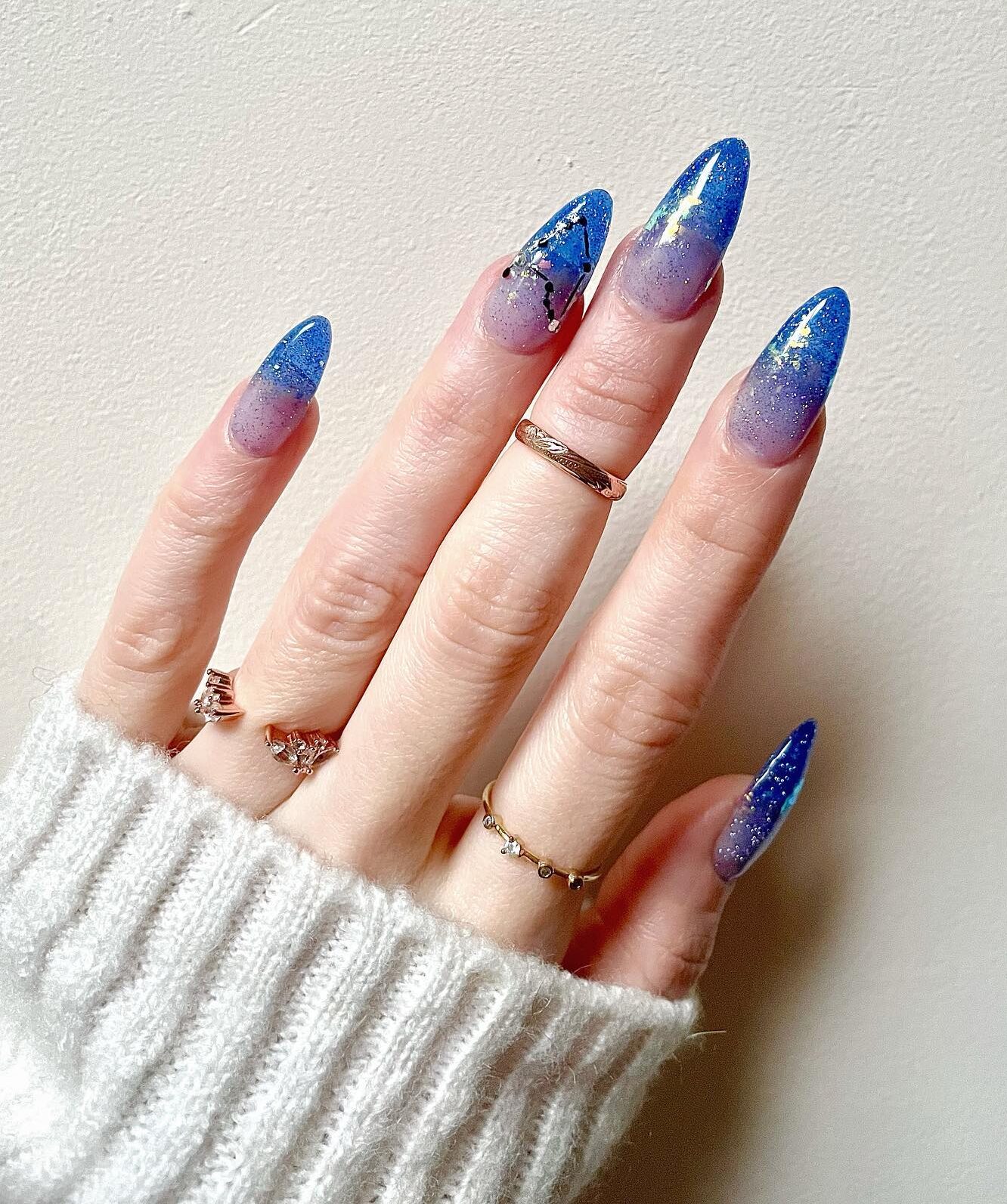 Vernis à ongles de couleur bleue scintillante avec motif d’ongle constellation Capricorne sur de longs ongles en amande