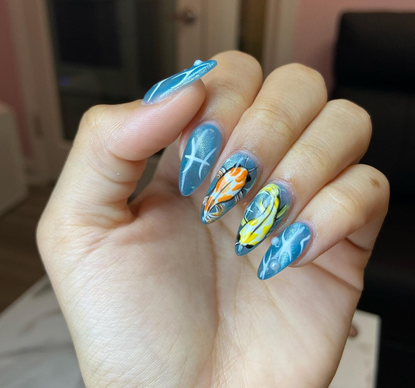 Vernis à ongles bleu métallisé avec symbole Poissons et ongles de poisson koi sur de longs ongles en amande