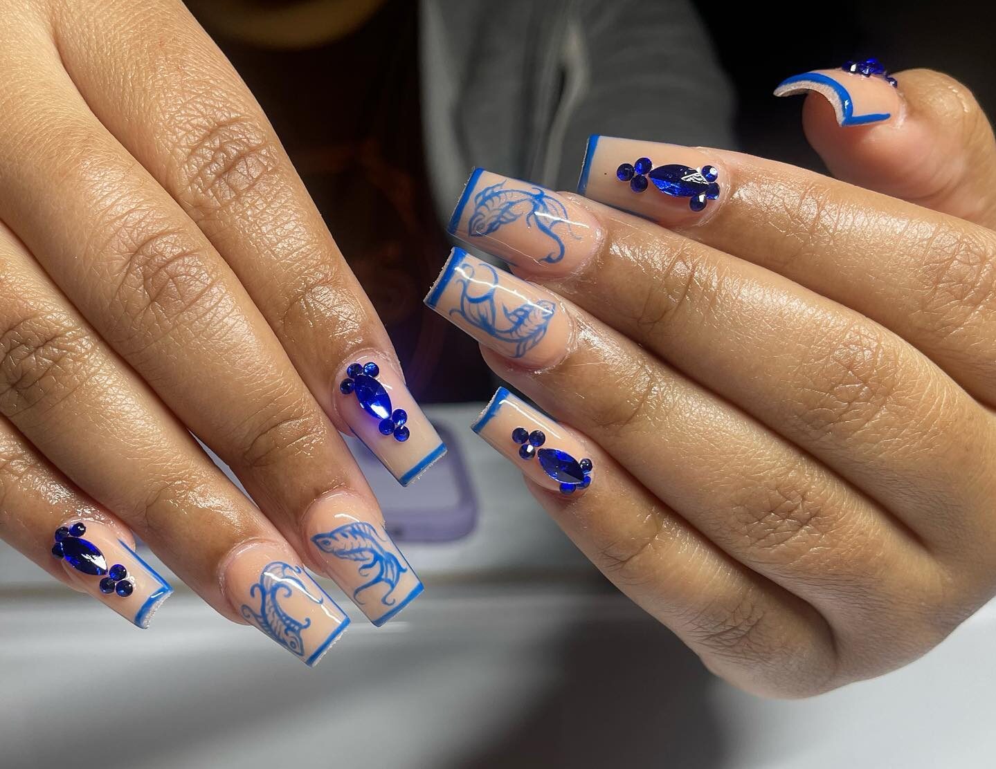 Couleur d’ongle nude avec des pointes françaises fines bleues, des gemmes bleues et des arts d’ongles de poisson koi bleu sur de longs ongles carrés effilés en acrylique