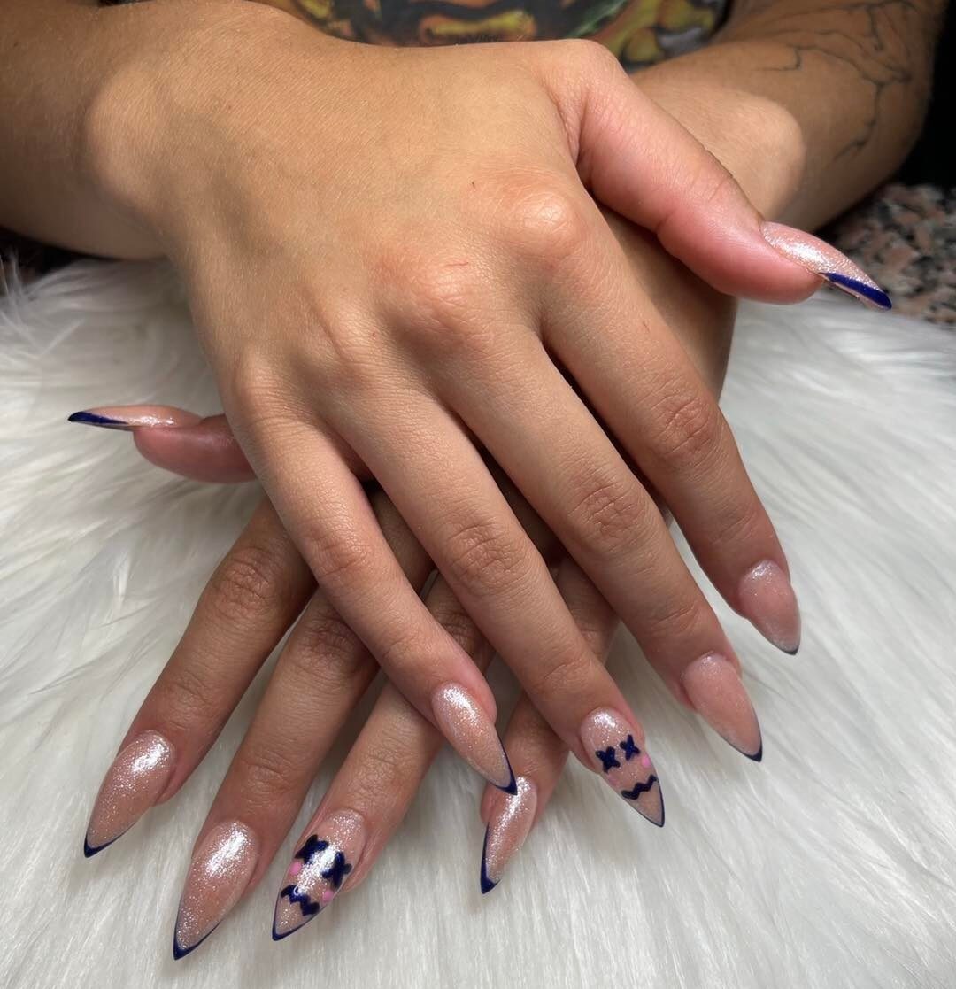 De longs ongles en acrylique en forme de talon aiguille avec des paillettes scintillantes, des pointes françaises fines bleues et un nail art bleu smiley