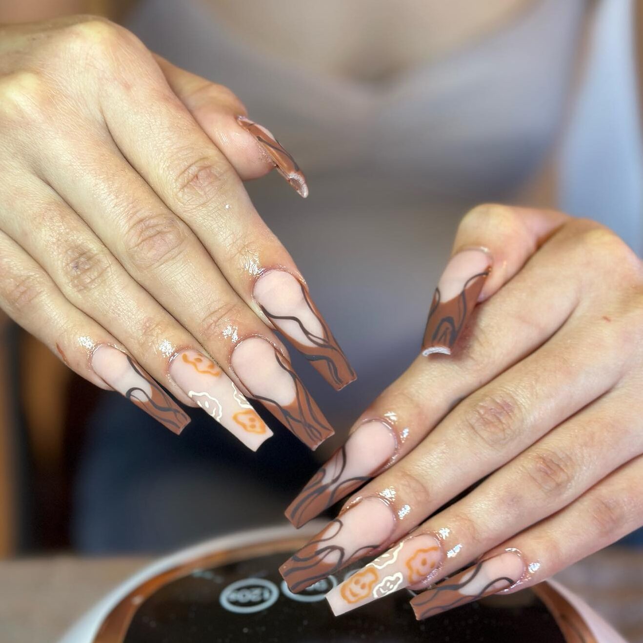 Pointes françaises brun foncé avec des tourbillons noirs et des visages souriants bruns nail art sur des ongles de cercueil super longs