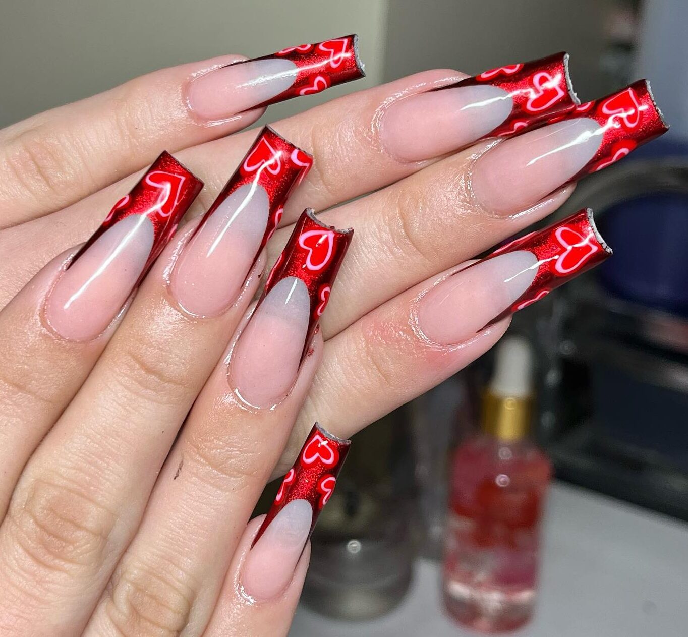 Ongles en acrylique de forme carrée longue et claire avec des pointes françaises rouge chrome vibrant et des coeurs nail art