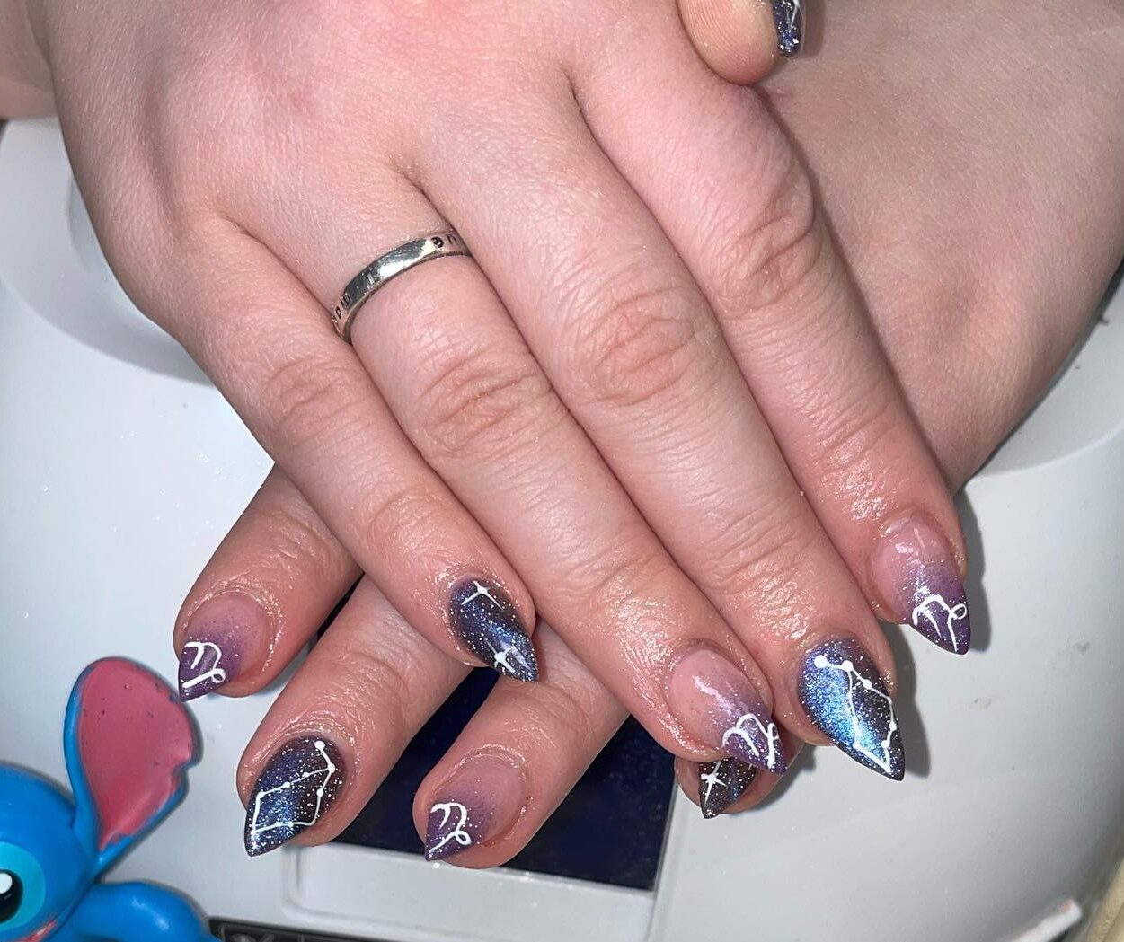 Vernis à ongles violet chromé avec symbole du Capricorne et motifs d’ongles constellation sur les ongles aiguilles moyens