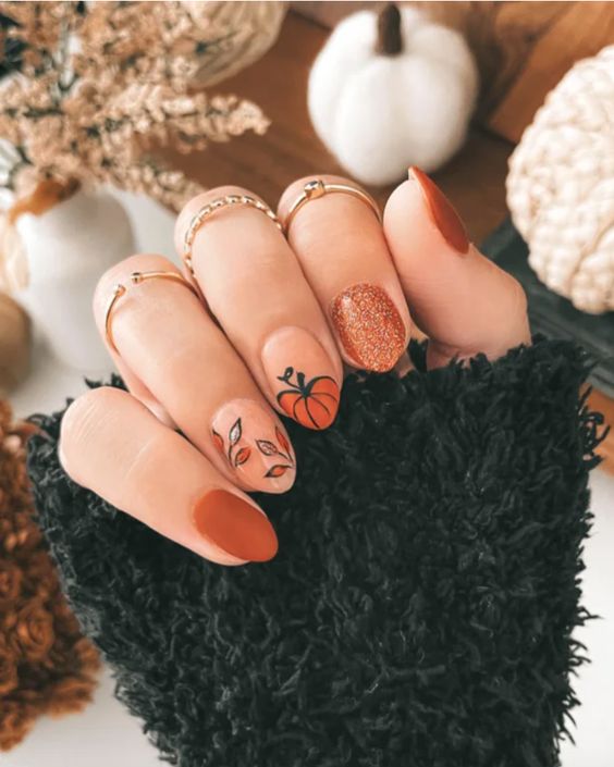 Vernis à ongles orange brûlé avec paillettes et nail art citrouille sur ongles courts en amande