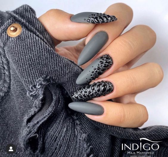 Vernis à ongles de couleur gris mat avec des nail arts gothiques foncés sur de longs ongles en amande