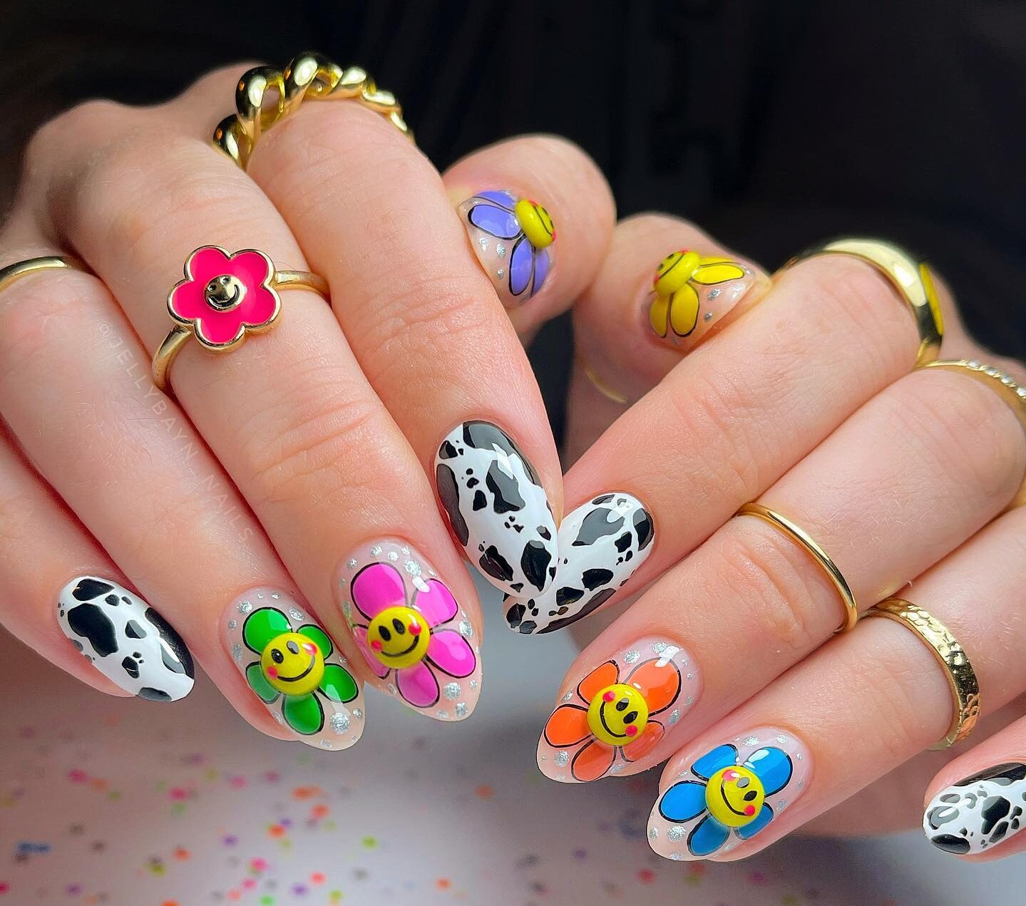 Motifs d’ongles de fleurs colorées, visages souriants jaunes et arts d’ongles imprimés de vache sur ongles en amande moyens