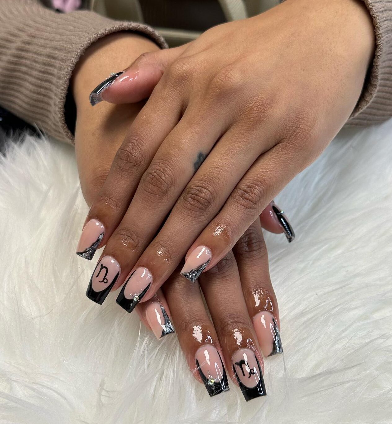 Ongles en acrylique de forme carrée moyenne avec des pointes françaises noires et un nail art symbole Capricorne