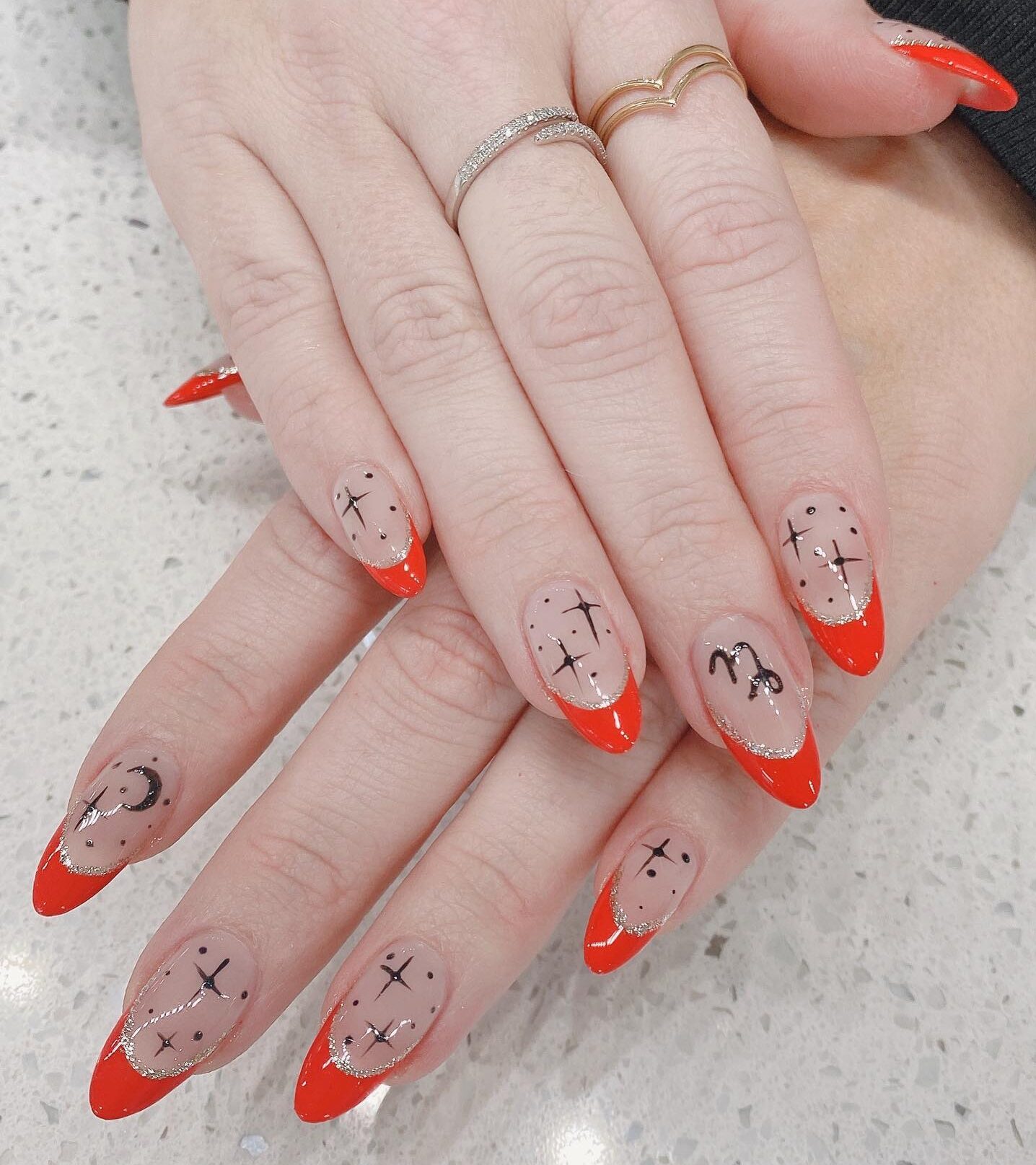 Ongles en acrylique transparent en forme d’amande avec des pointes françaises rouge vif et des éléments célestes nail arts