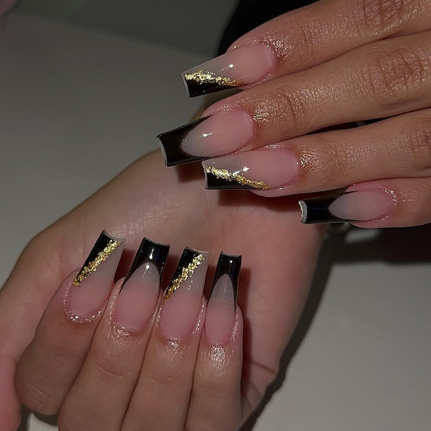 Longs ongles en acrylique de forme carrée effilée claire avec des pointes françaises noires et des contours en feuille d’or