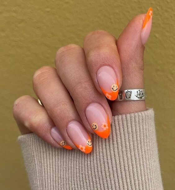 Pointes françaises orange vif avec des fleurs et des visages souriants nail art sur ongles courts et ronds