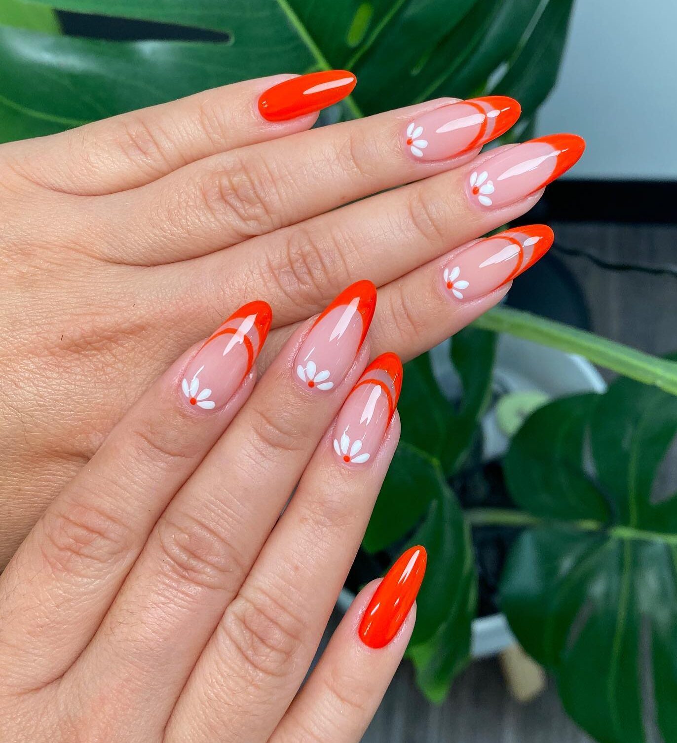 Ongles longs et ronds en acrylique clair avec des pointes françaises orange vif et des motifs d’ongles à fleurs blanches