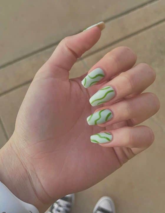 Vernis à ongles vert pâle au fini mat avec des tourbillons verts sur des ongles carrés effilés moyens