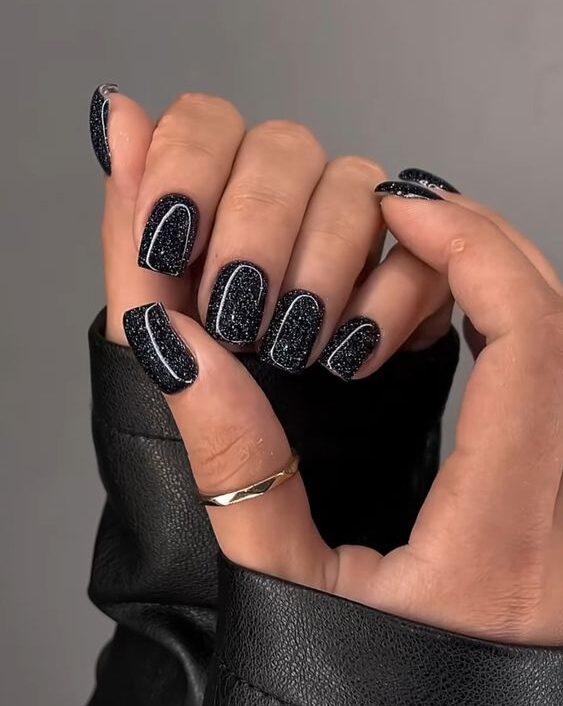 Vernis à ongles noir brillant avec des paillettes argentées sur des ongles carrés courts