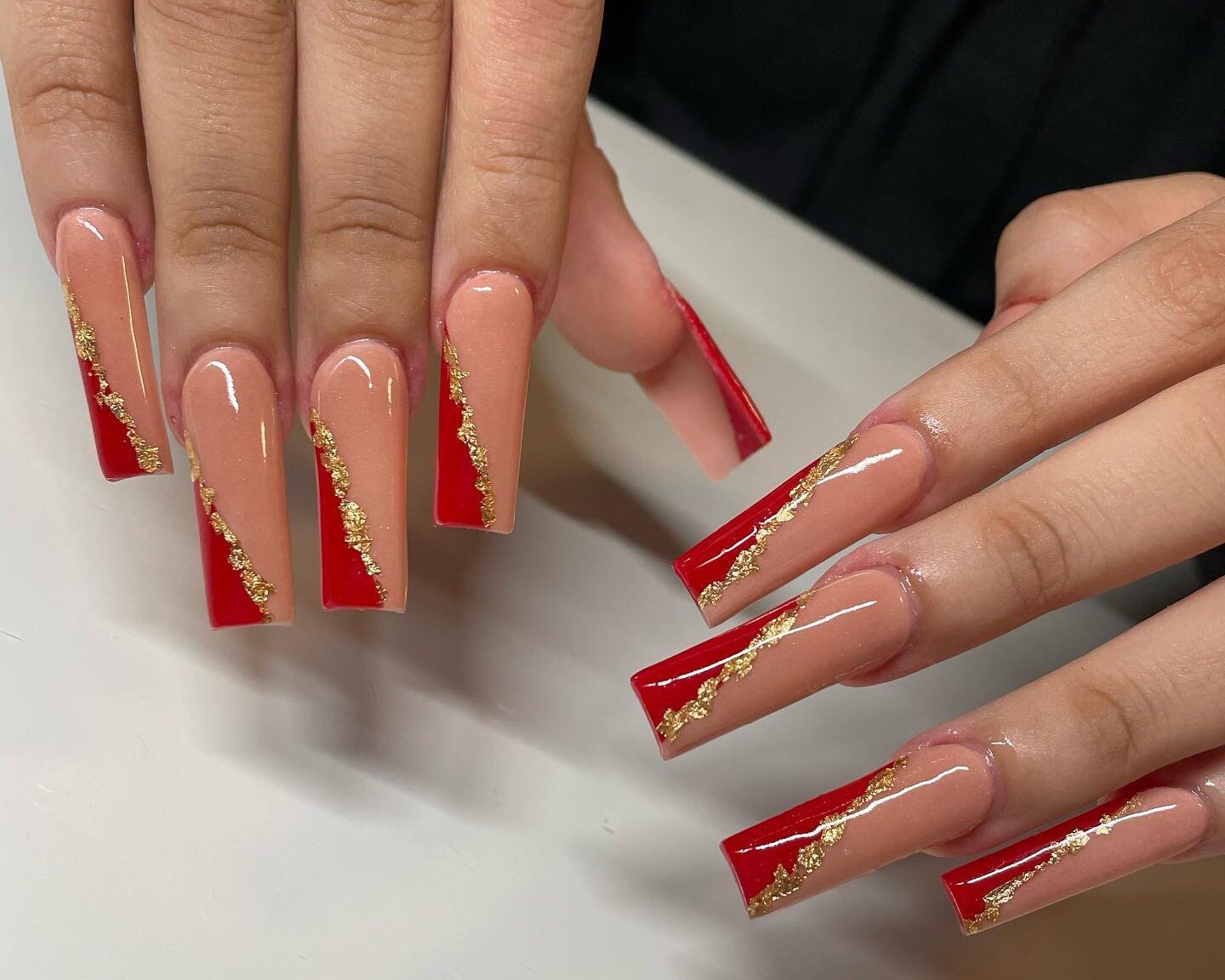 Vernis à ongles pêche avec des pointes françaises rouges obliques et une feuille d’or sur des ongles carrés super longs