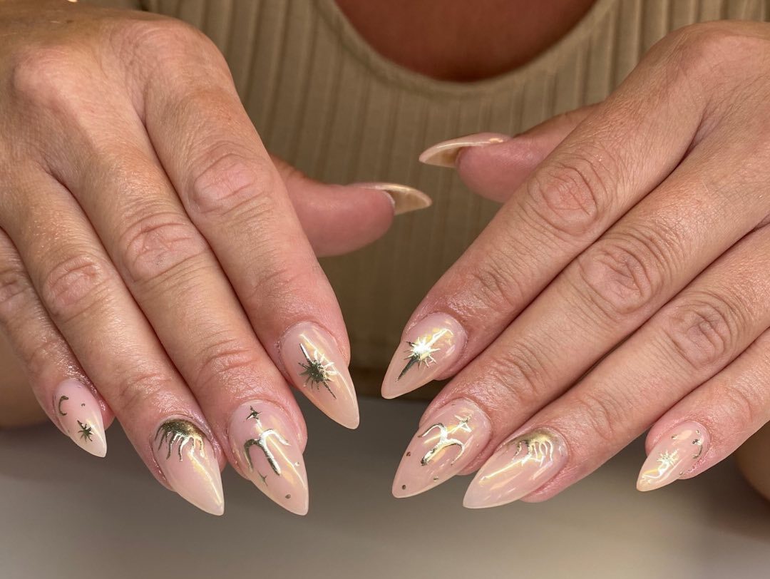 Signe Bélier or et éléments célestes nail arts sur de longs ongles en acrylique en forme de stiletto