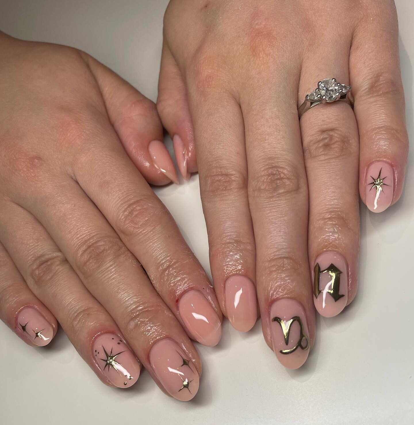 Vernis à ongles de couleur naturelle avec des éléments célestes dorés métalliques sur des ongles ronds moyens