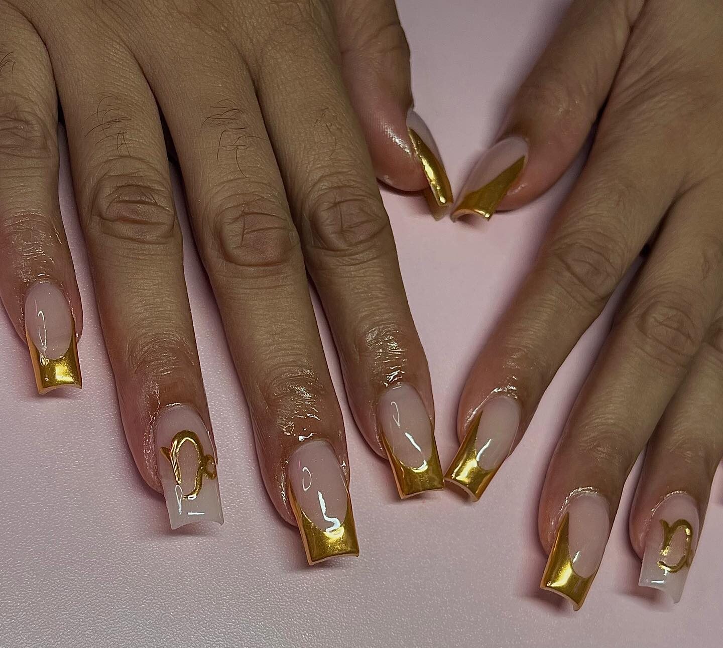 Ongles en acrylique de forme carrée moyenne avec des pointes françaises dorées métalliques et un nail art symbole Capricorne