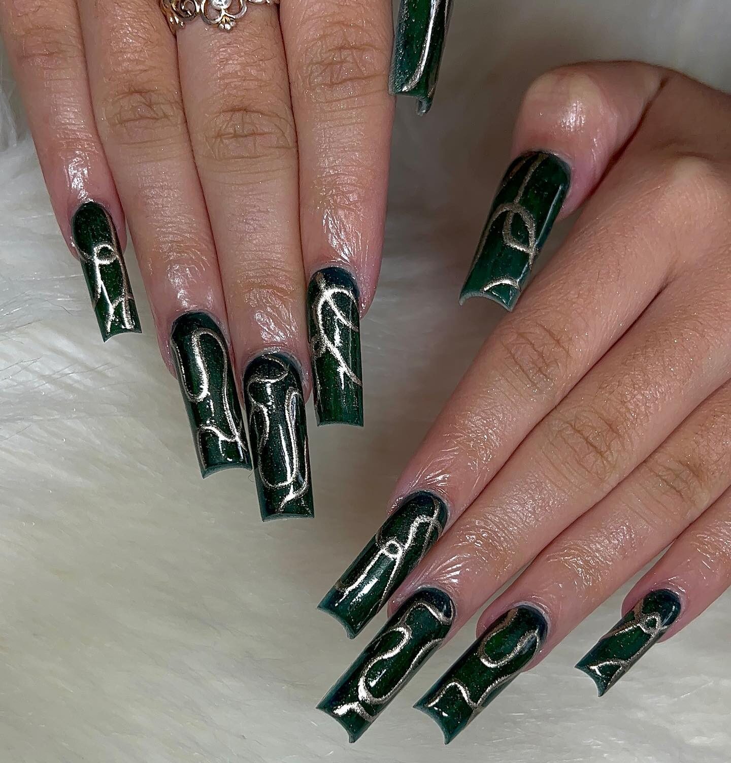 Couleur des ongles vert foncé avec des motifs tourbillonnants argentés métalliques sur de longs ongles carrés en acrylique