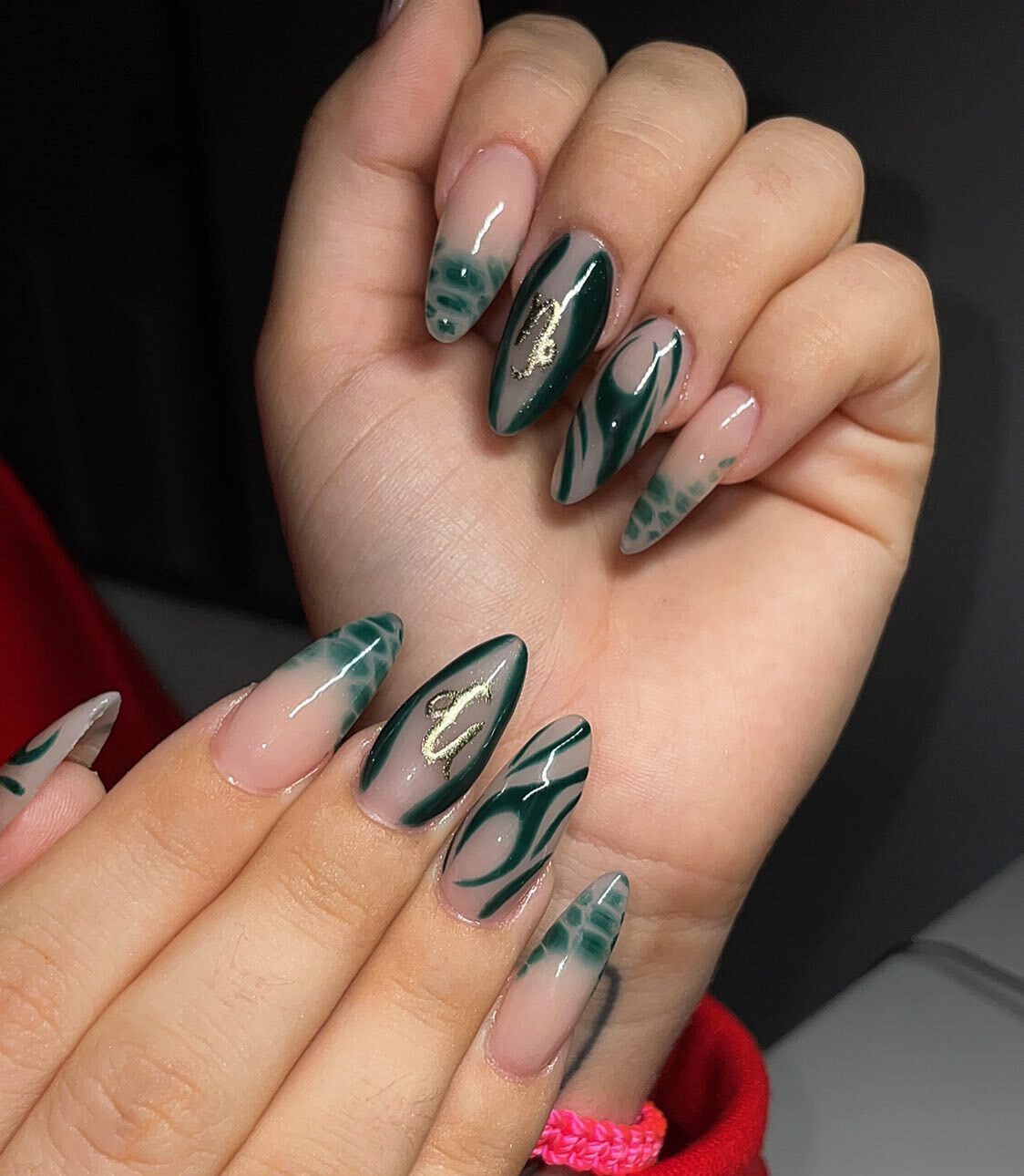 Ongles longs en acrylique en forme d’amande avec des nail arts abstraits vert foncé et le symbole du Capricorne