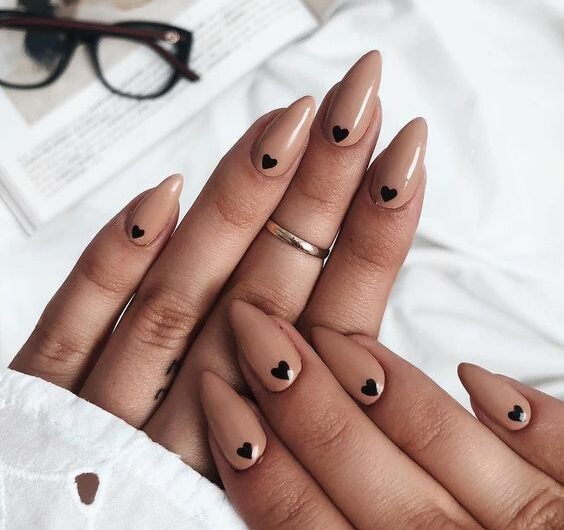 Couleur d’ongle nude avec des cœurs noirs nail art sur ongles amandes moyens