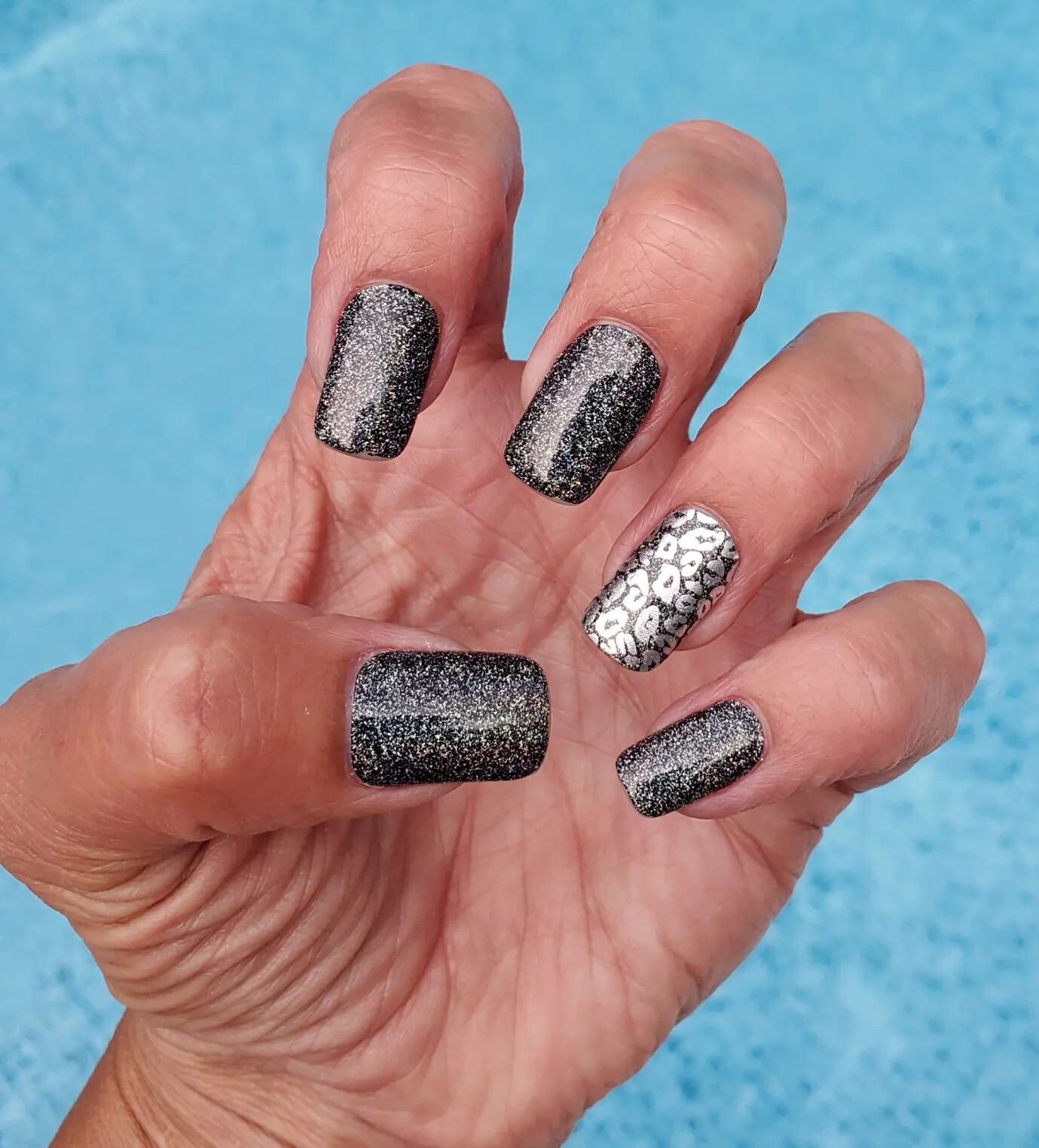 Vernis à ongles noir avec paillettes argentées et nail art imprimé léopard argenté sur ongles carrés moyens