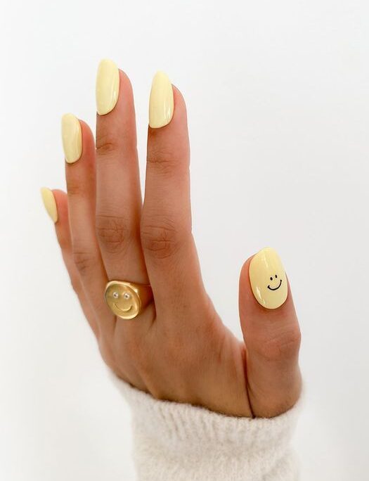 Couleur d’ongle jaune pastel avec nail art smiley sur des ongles ronds courts