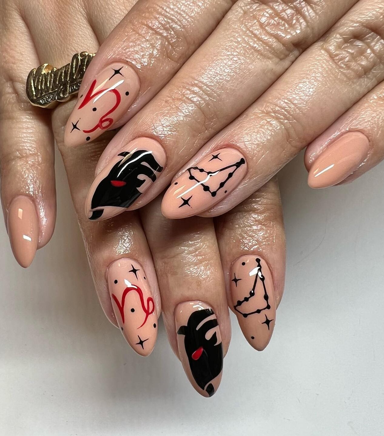 Vernis à ongles nude avec symbole du Capricorne et motifs d’ongles constellations sur ongles en amande moyens