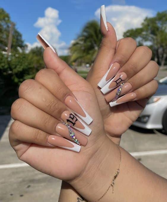 Vernis à ongles nude avec des pointes françaises blanches, signe Gémeaux, et strass nail arts sur de longs ongles de cercueil