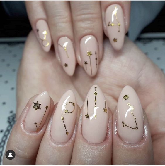 Couleur d’ongle nude avec signe Taureau doré et éléments célestes nail arts sur ongles longs en amande