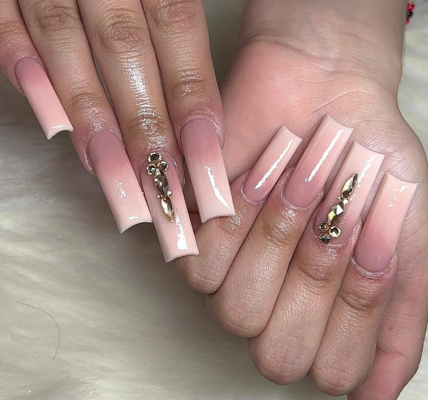 Effet ombré nude en finition brillante avec des pierres précieuses sur des ongles carrés super longs