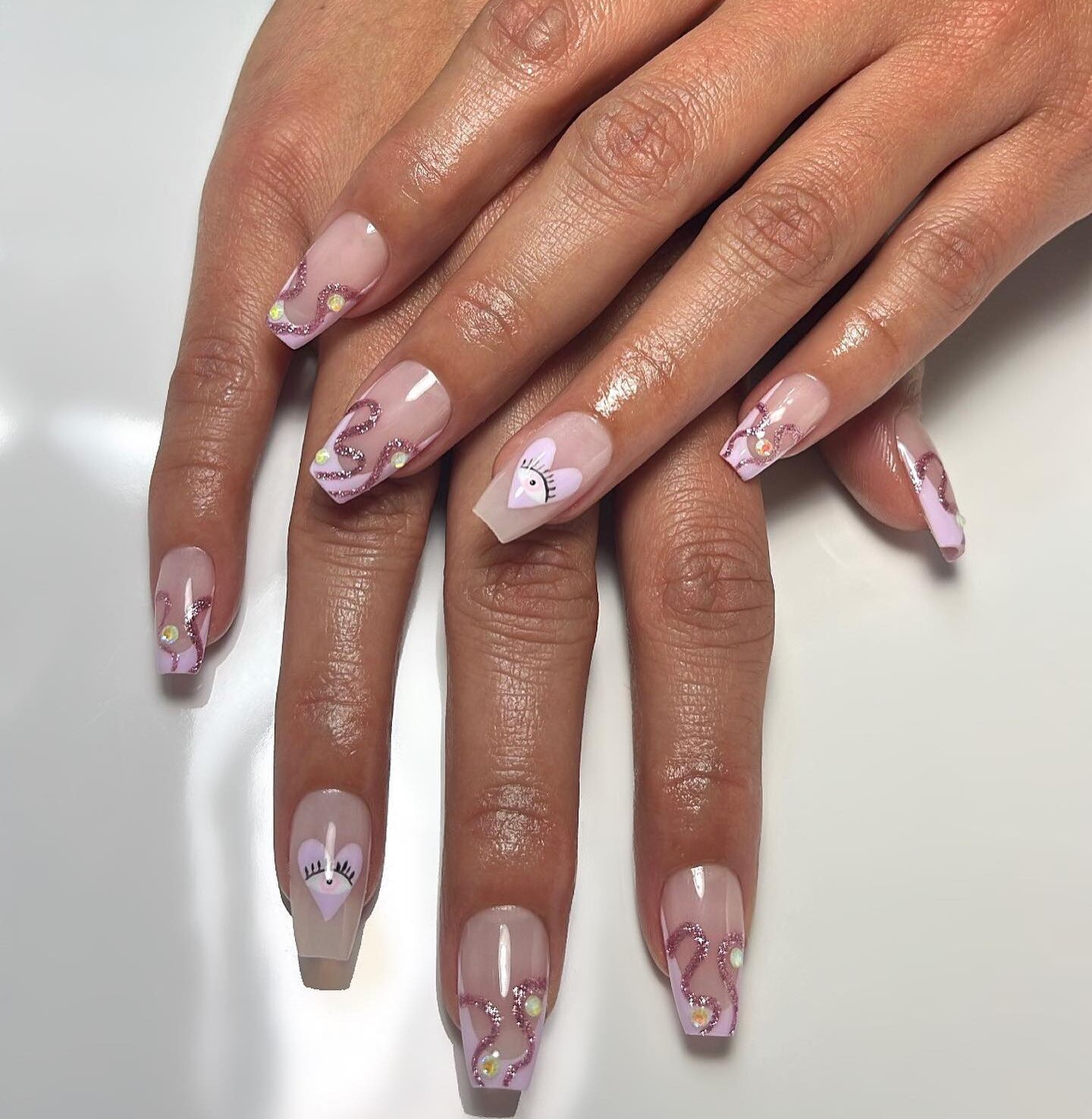 Ongles en acrylique transparents en forme de cercueil avec des pointes françaises rose clair, des tourbillons scintillants et un art des ongles du mauvais œil