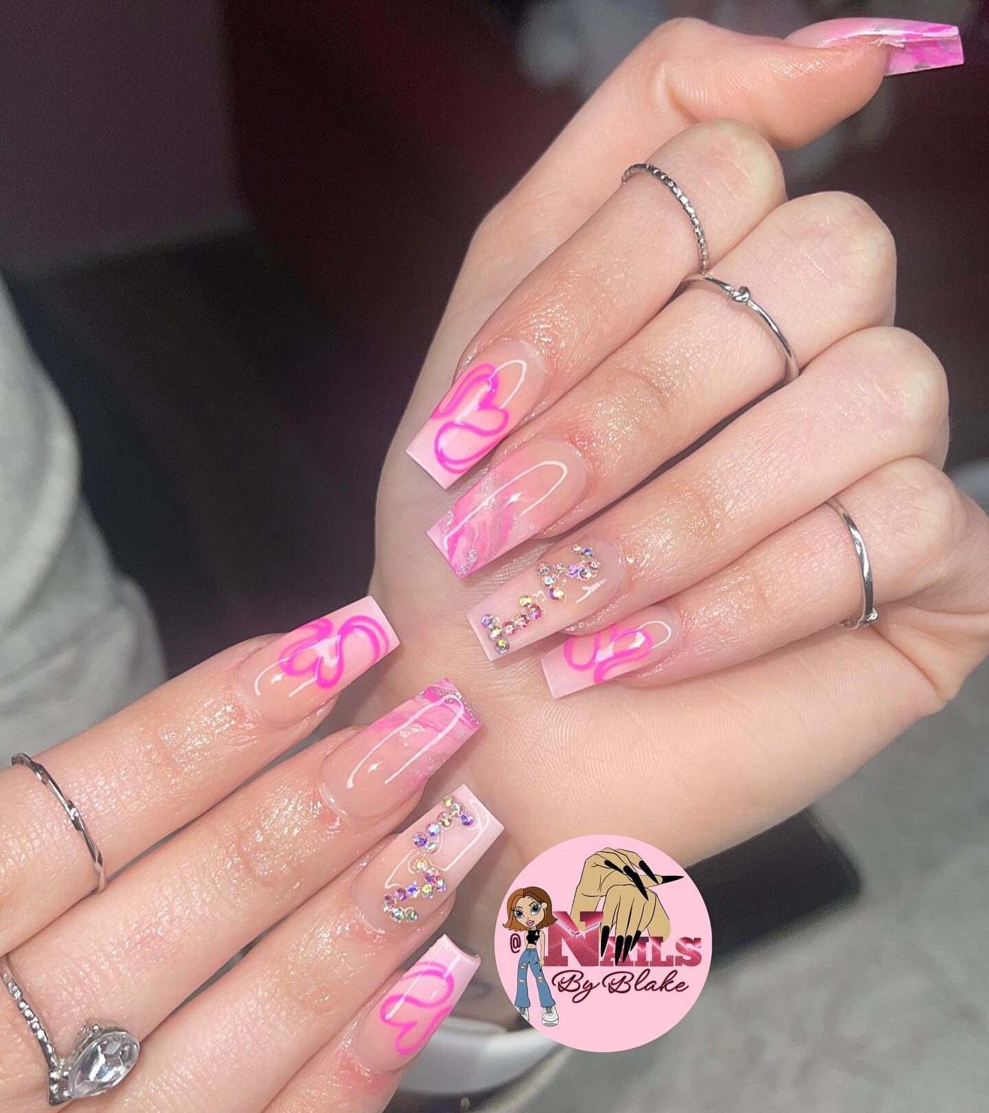 Longs ongles en acrylique coniques clairs et effilés en forme de carré avec des tourbillons roses, un nail art en marbre rose et des motifs d’ongles en strass