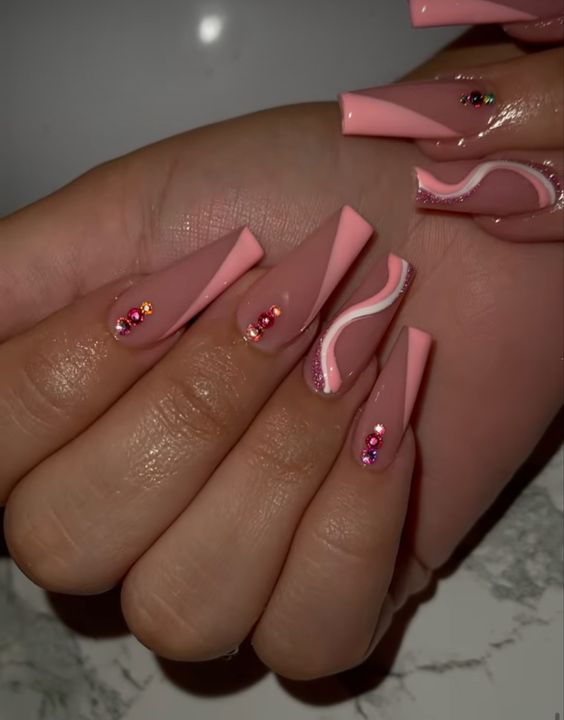 Pointe française inclinée rose bébé et tourbillons avec des strass roses sur de longs ongles en acrylique en forme de cercueil