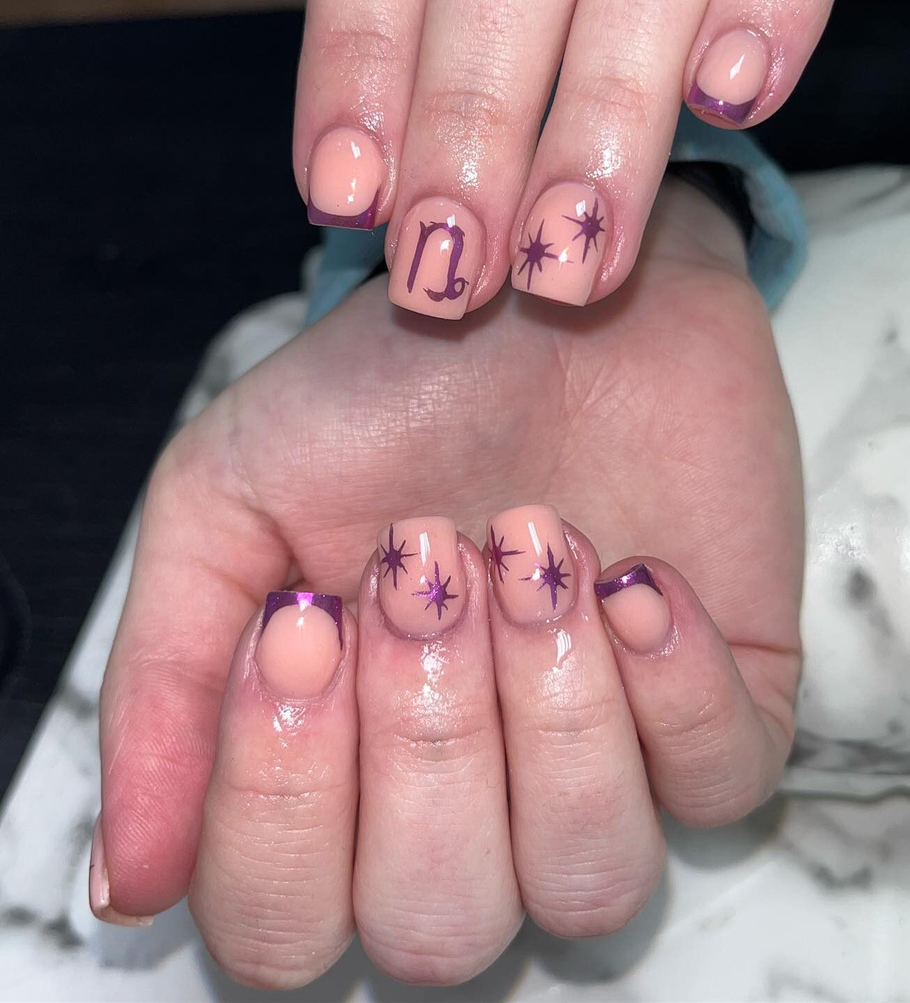 Vernis à ongles nude avec pointes françaises violettes et nail art symbole Capricorne sur ongles carrés courts