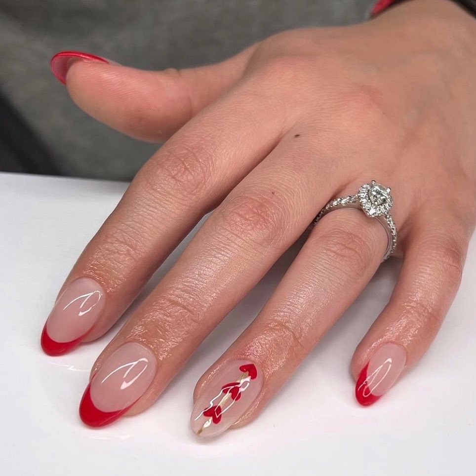 Ongles rouges à pointe française avec motif de cœur sur l’annulaire