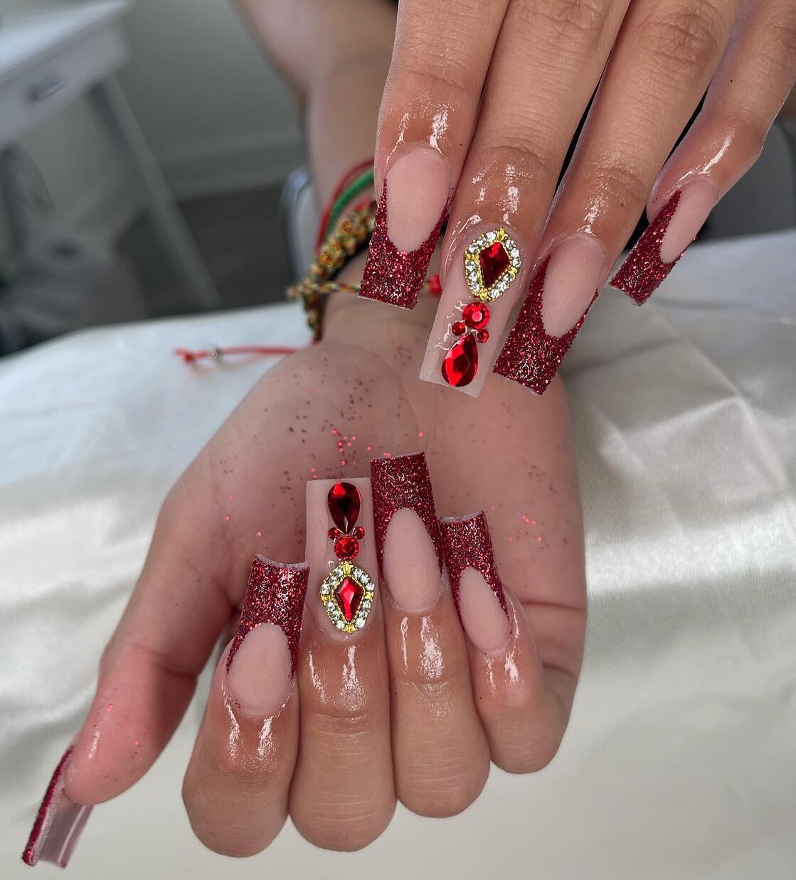 Vernis à ongles de couleur nude avec des pointes françaises rouges scintillantes, du bling 3D et des strass sur de longs ongles carrés