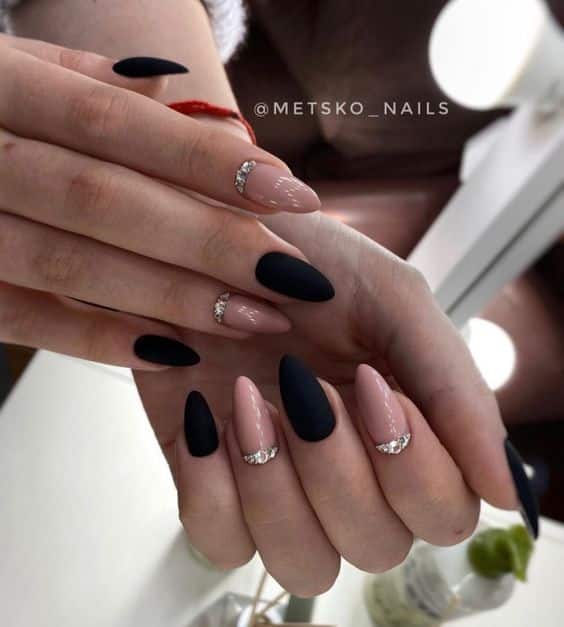 Couleurs d’ongles noir mat et nude brillant avec strass sur les ongles longs en amande