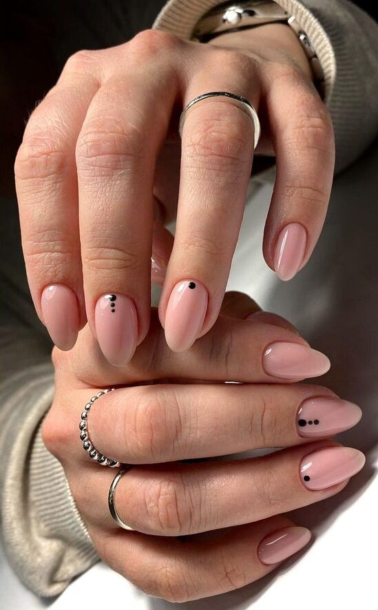 Couleur d’ongle nude avec des petits points noirs nail art sur ongles ronds moyens