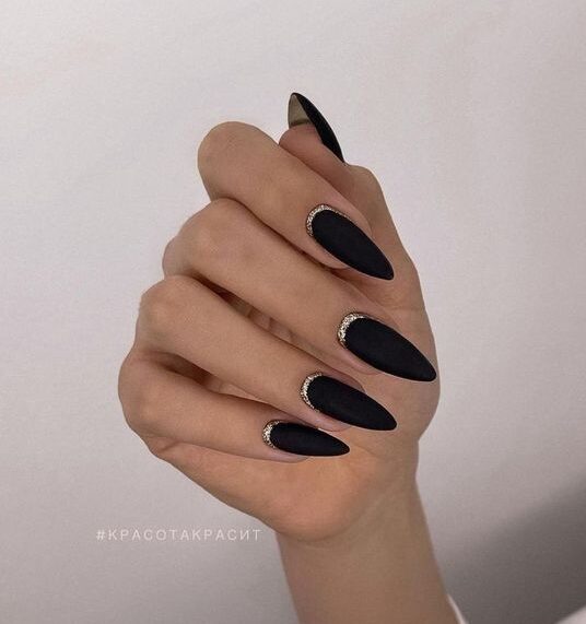 Vernis à ongles noir mat avec des paillettes argentées sur les ongles longs en amande