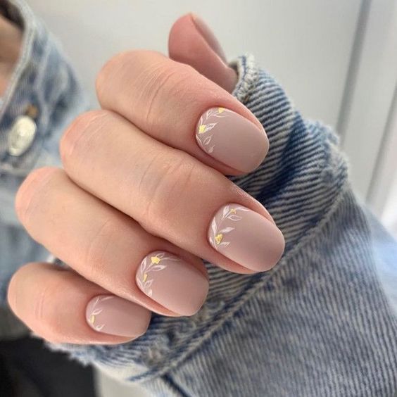 Couleur d’ongle beige en finition mate avec des feuilles nail art sur ongles carrés courts et effilés