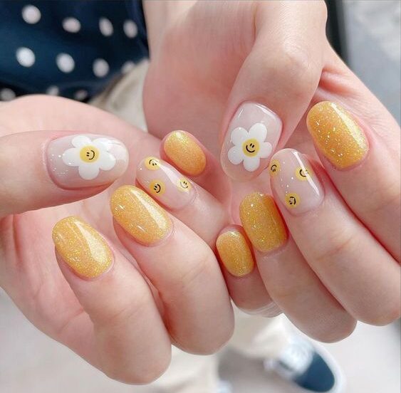 Couleur d’ongles jaune scintillant avec des fleurs blanches et des smileys jaunes sur des ongles ronds courts